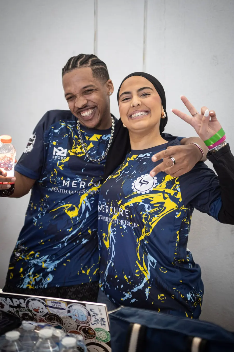 Deux bénévoles en maillot des Paramètres, souriants, à la table d'accueil