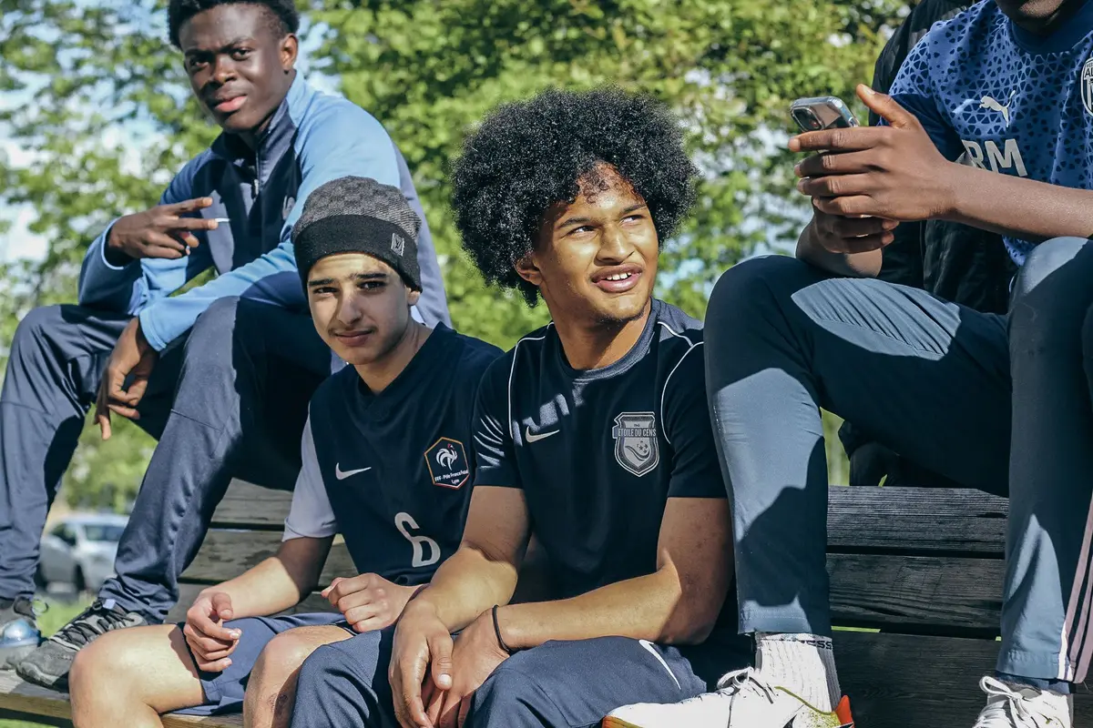 Des joueurs assis sur un banc suivent un match, dont l'un en maillot de l'Étoile du Cens