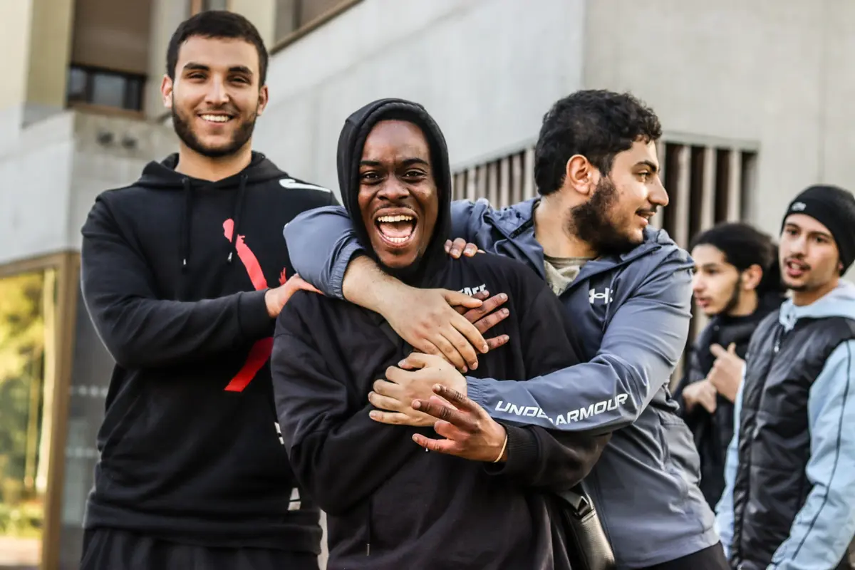 Trois jeunes hommes rient ensemble au pied d'un immeuble du quartier