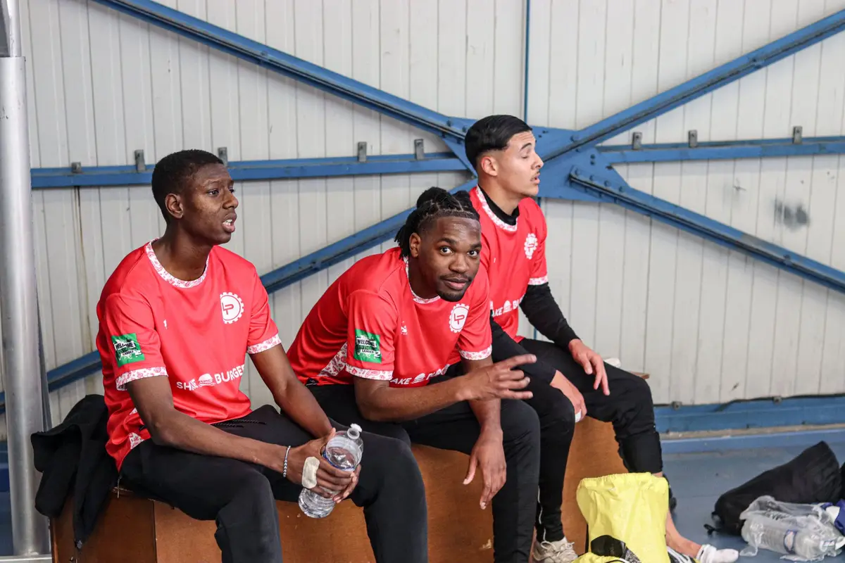 Trois joueurs en maillots rouges assis sur un banc du gymnase