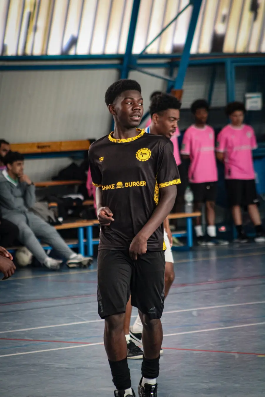 Un joueur en maillot noir et jaune floqué Shake Burger, sur le terrain du gymnase