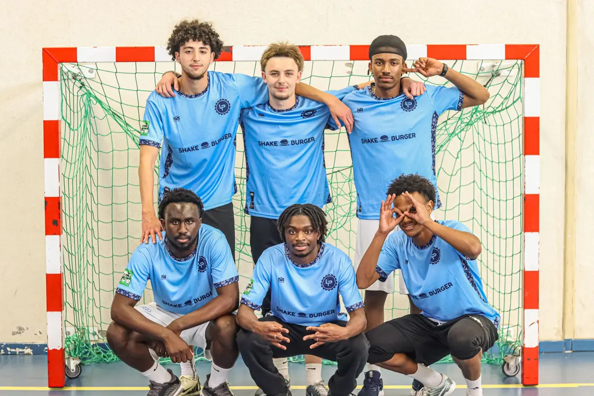Une équipe en maillots bleu ciel floqués Shake Burger pose devant un but de handball