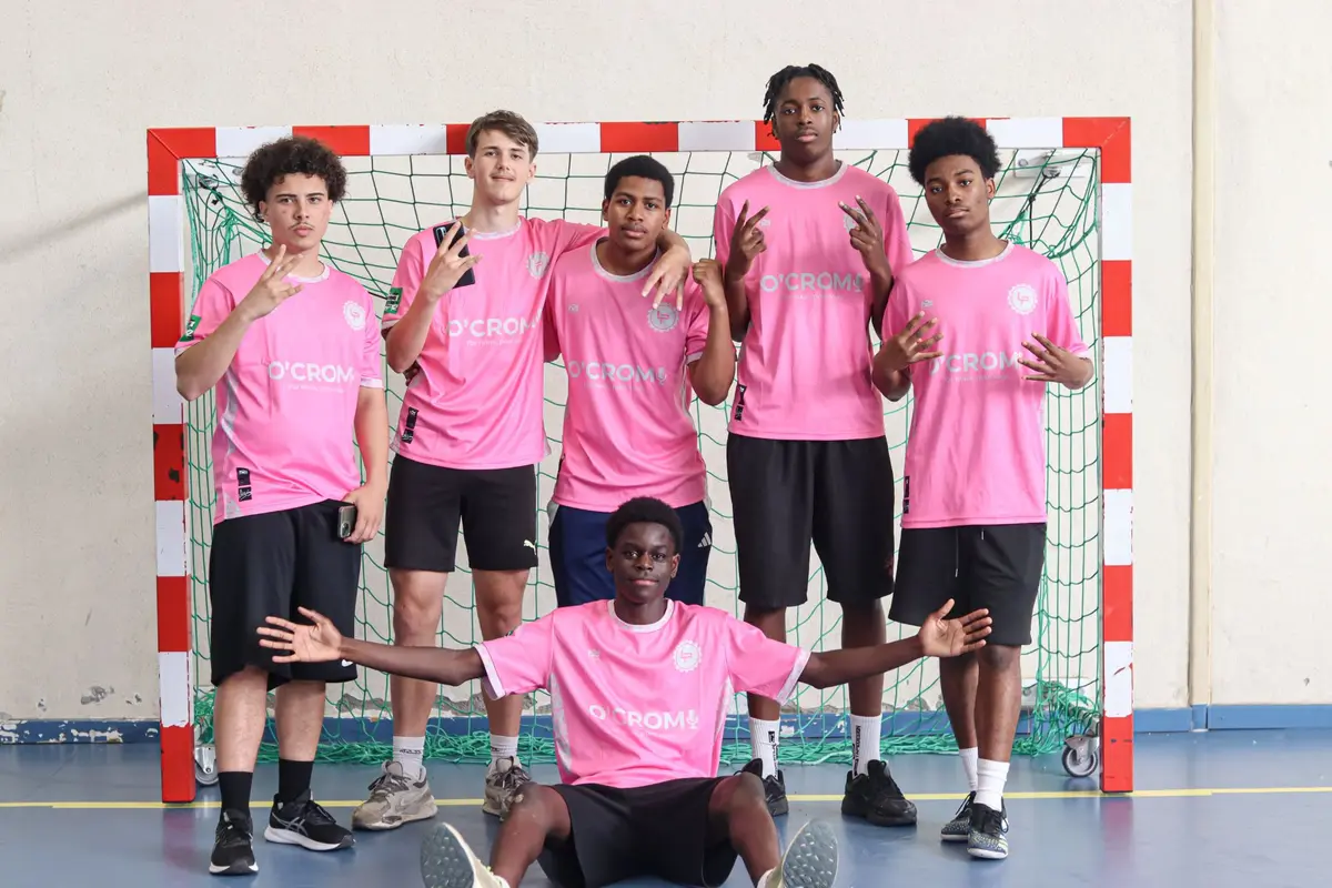 Une équipe en maillots roses floqués O'Crom pose devant un but de handball