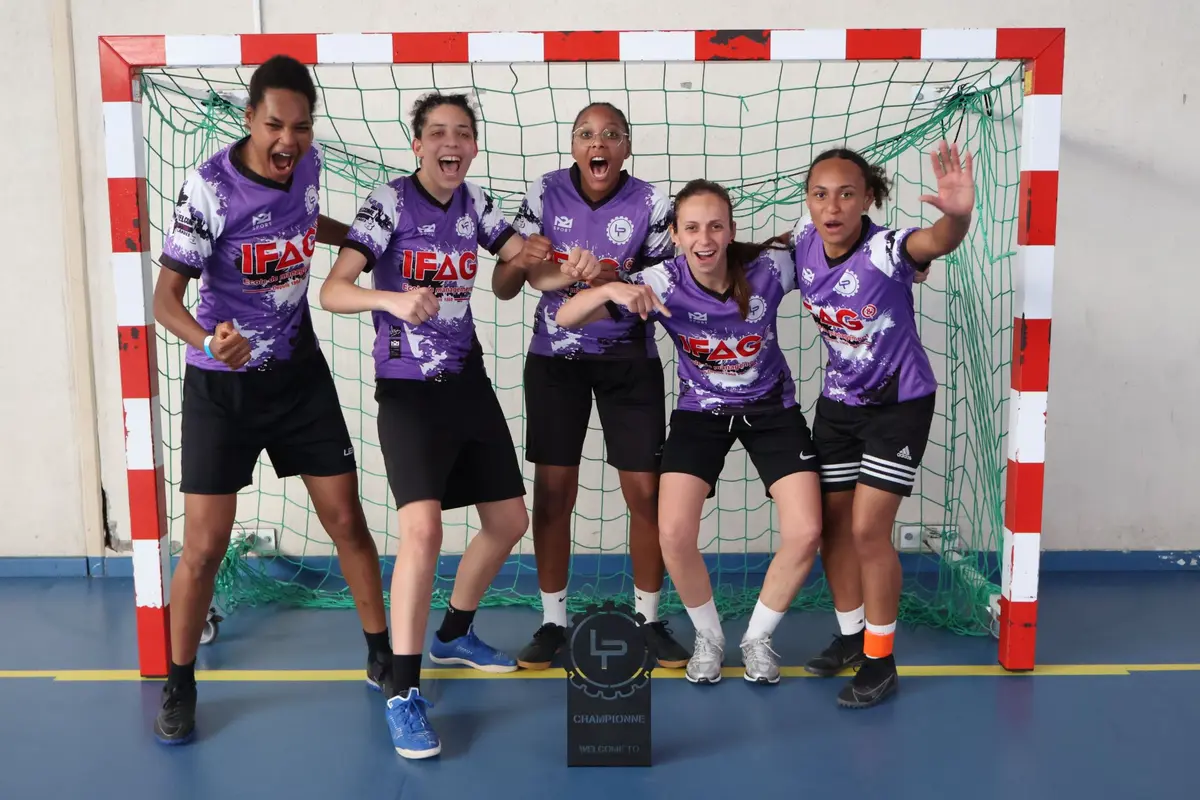 Cinq joueuses en maillots violets célèbrent devant un but, avec le trophée de championne